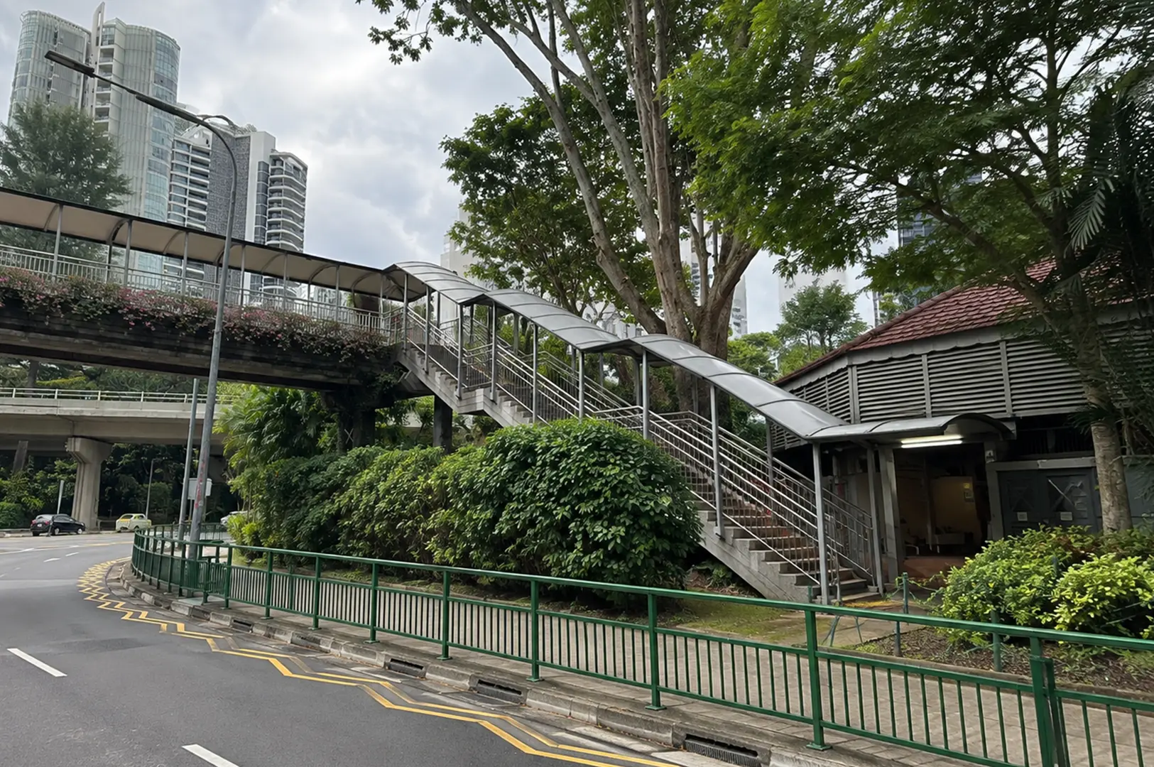 Exterior view of the food centre with a covered pedestrian staircase, greenery, and surrounding high-rise buildings.