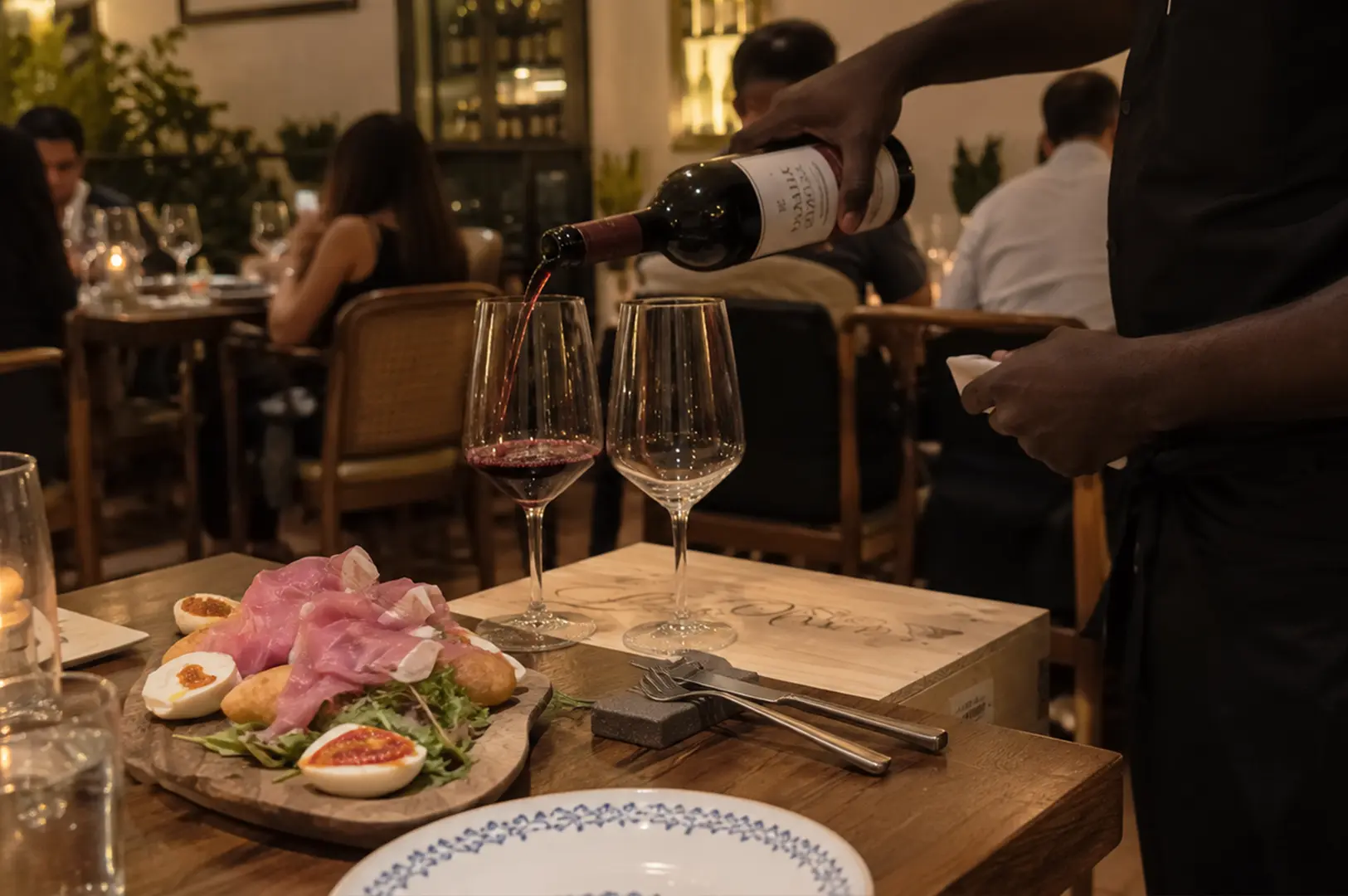 Server pouring red wine beside an Italian charcuterie platter in a cozy dining room.