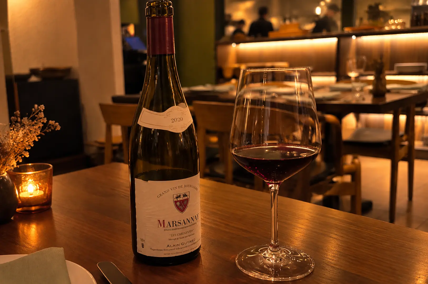 Bottle of Marsannay red wine with a filled wine glass on a candlelit restaurant table.