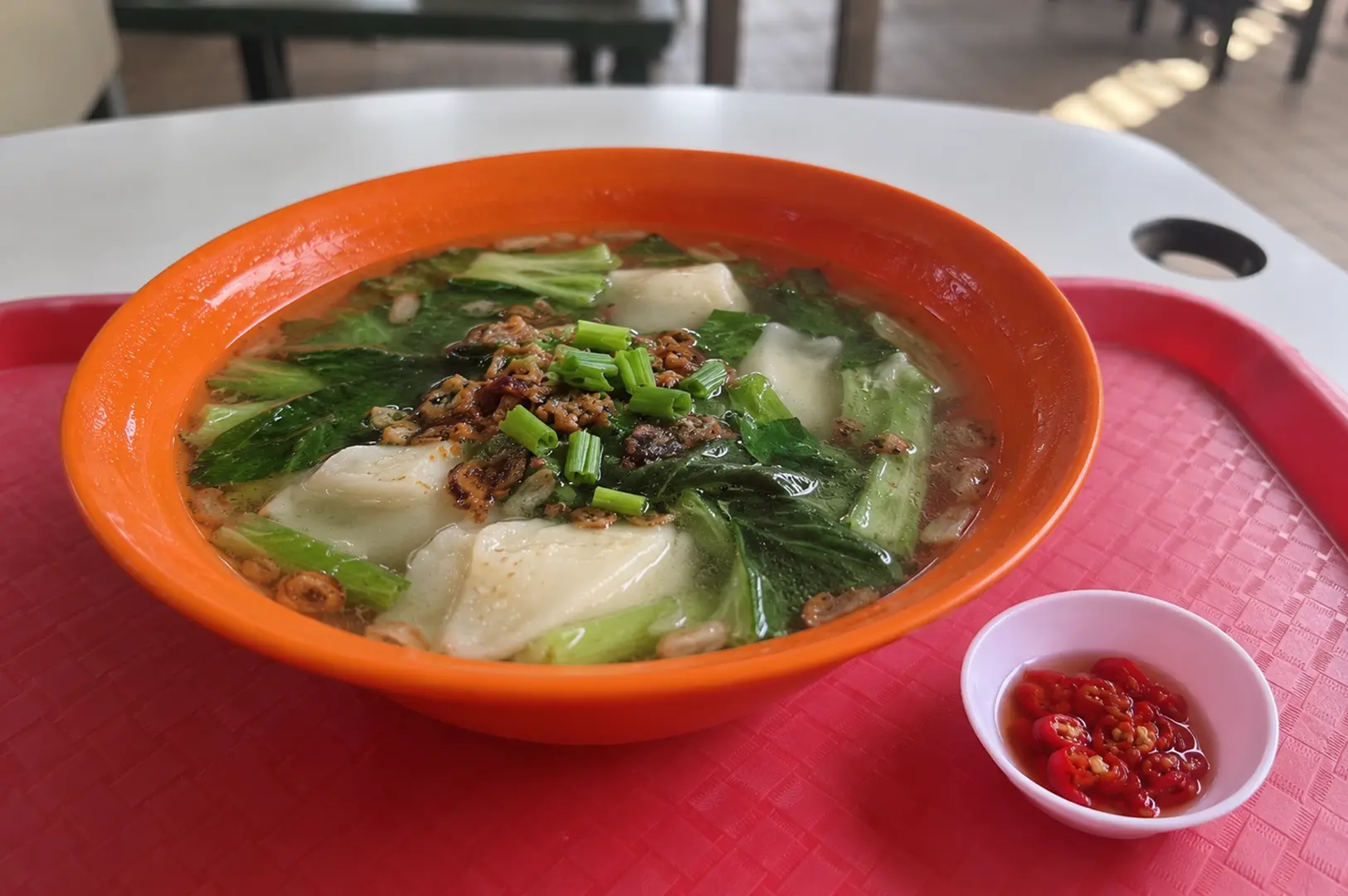Tender fish bowl in clear broth with leafy greens, crispy toppings, and sliced red chilies on the side.