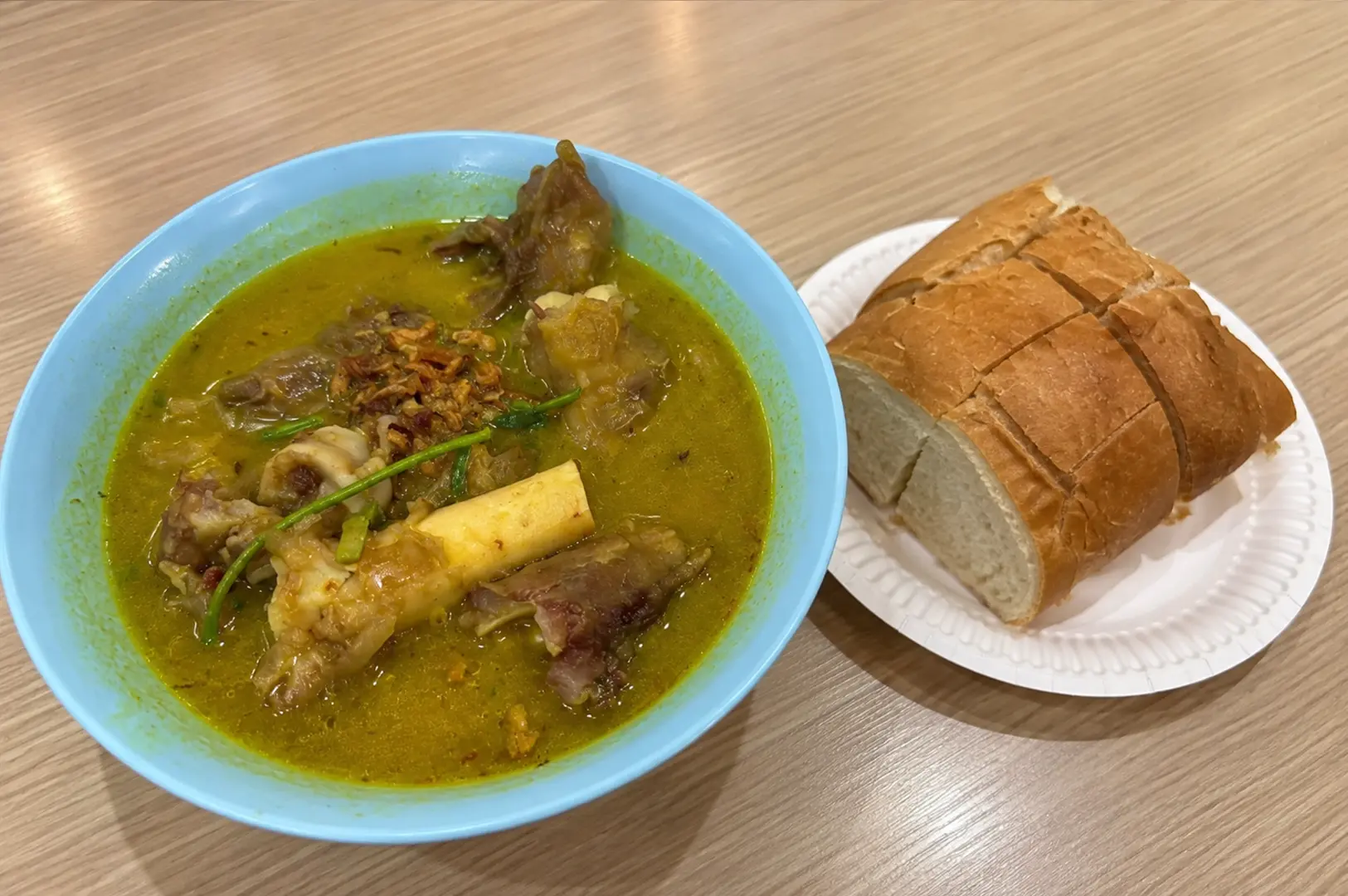 A bowl of rich mutton ribs soup served alongside sliced French loaf.