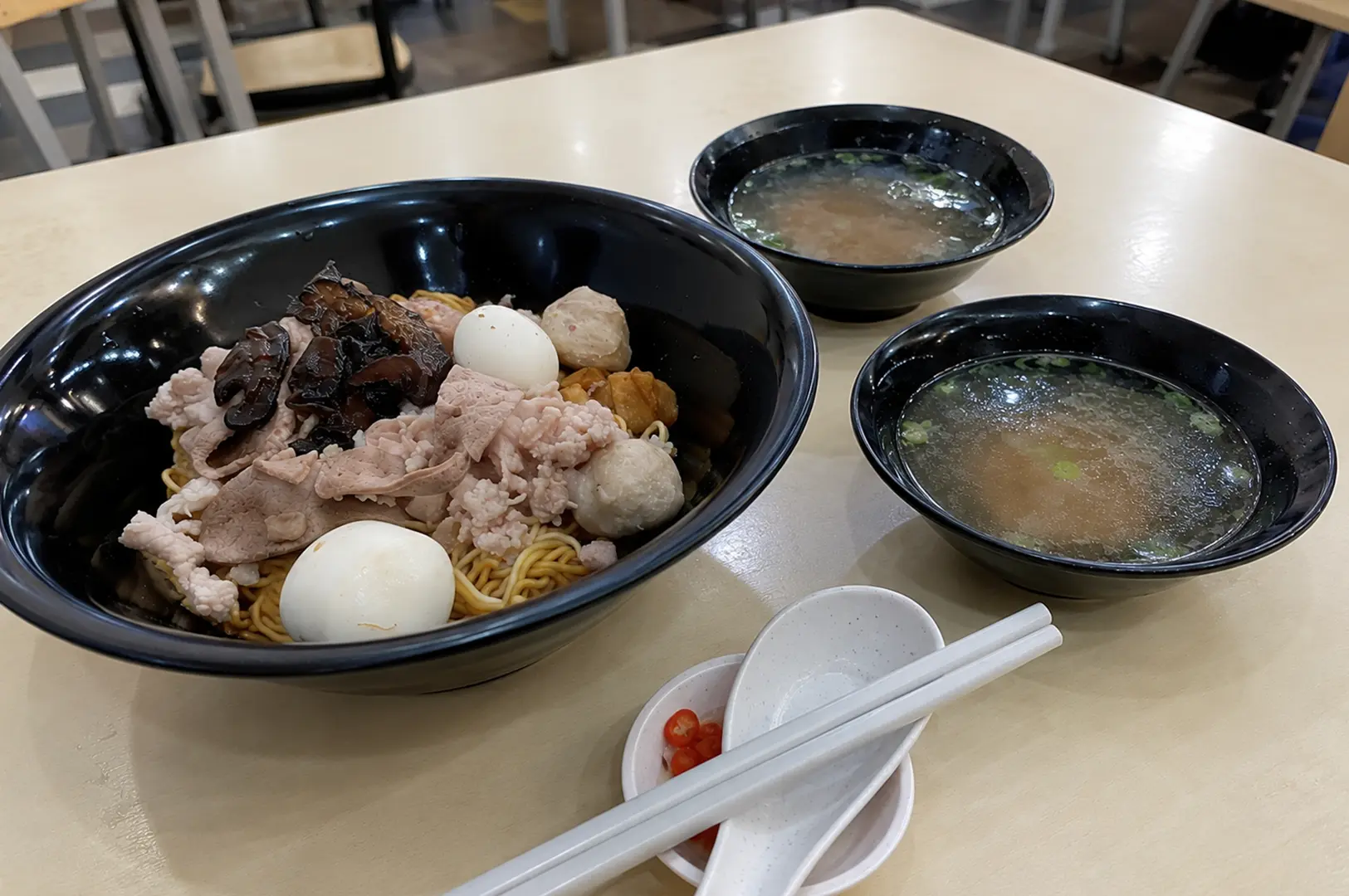 Dry noodles topped with sliced pork, fish balls, mushrooms, and boiled eggs with clear soup.