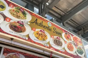 A Thai food stall displays its menu of dishes beneath a sign reading “Authentic Siam.”
