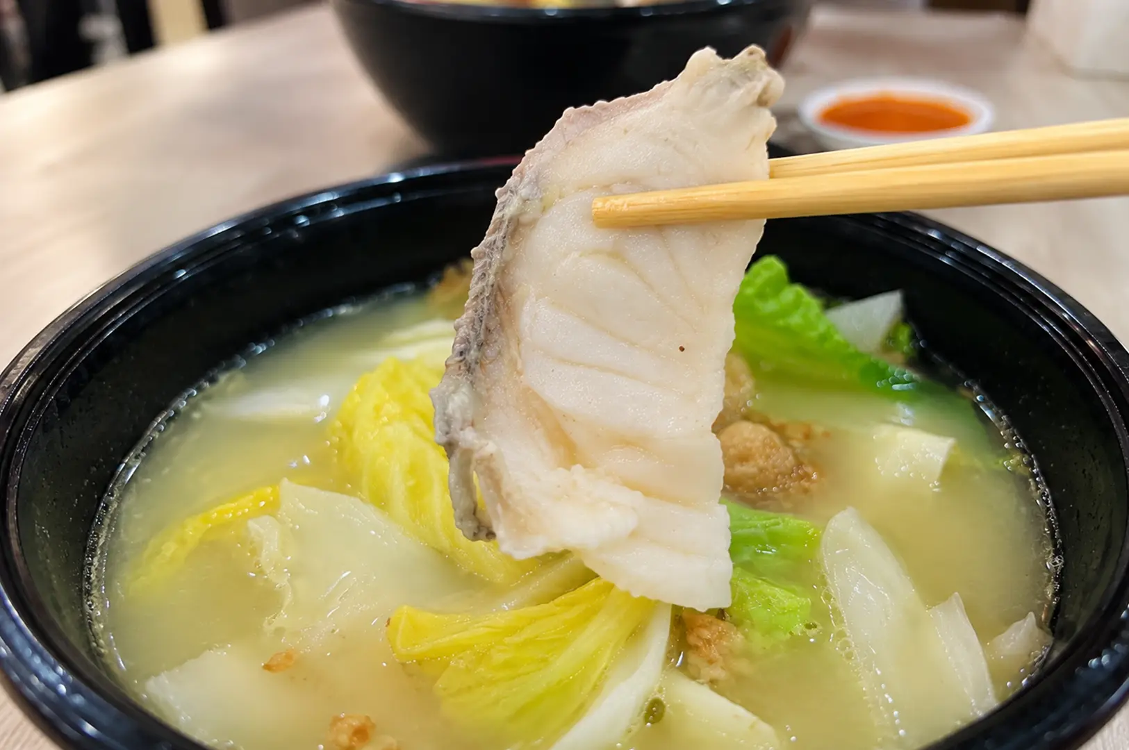 Fish soup with a large slice of tender white fish held above a bowl of clear broth and vegetables.