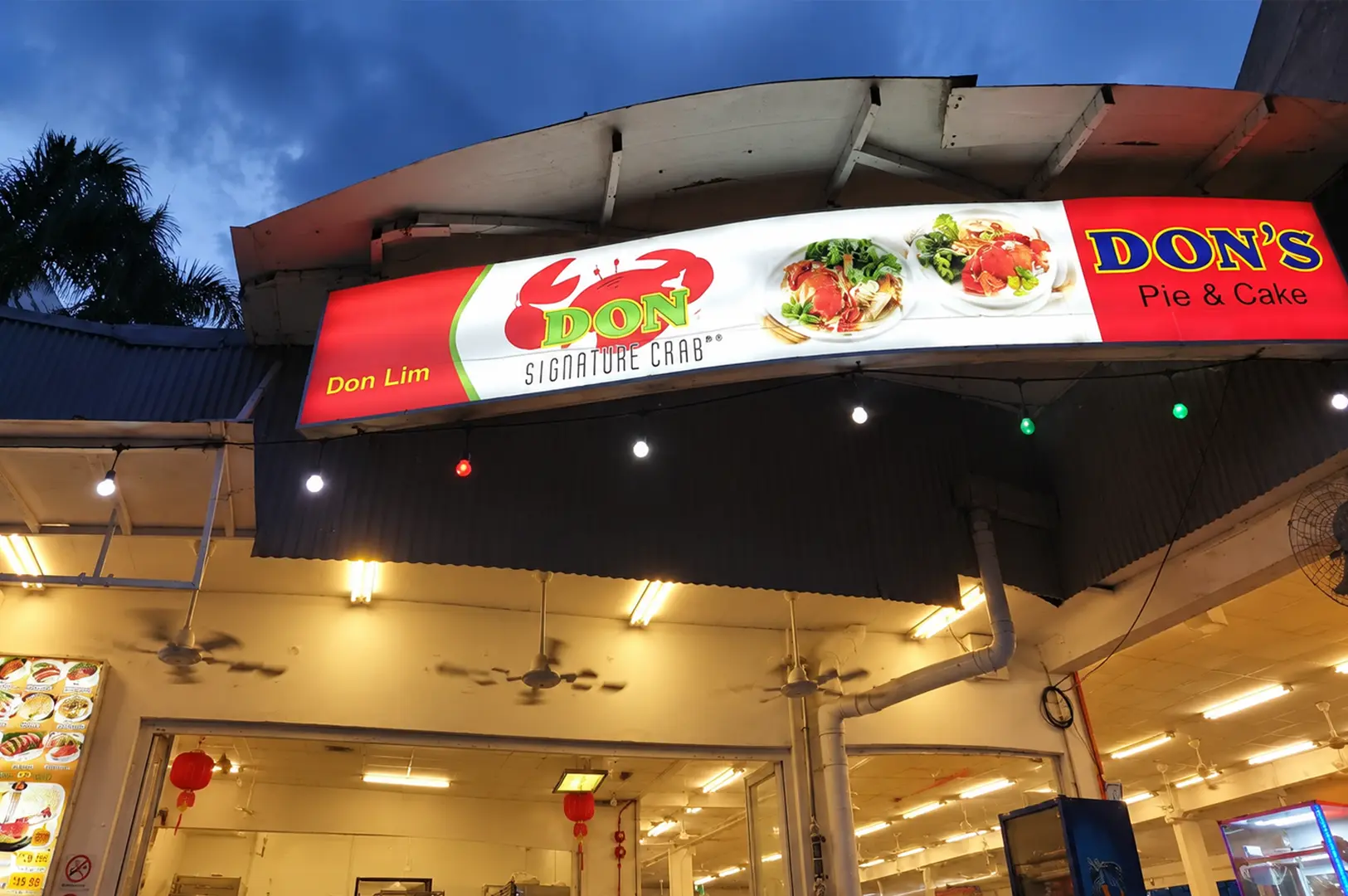 Don Signature Crab restaurant sign illuminated against a blue evening sky above the open dining area.