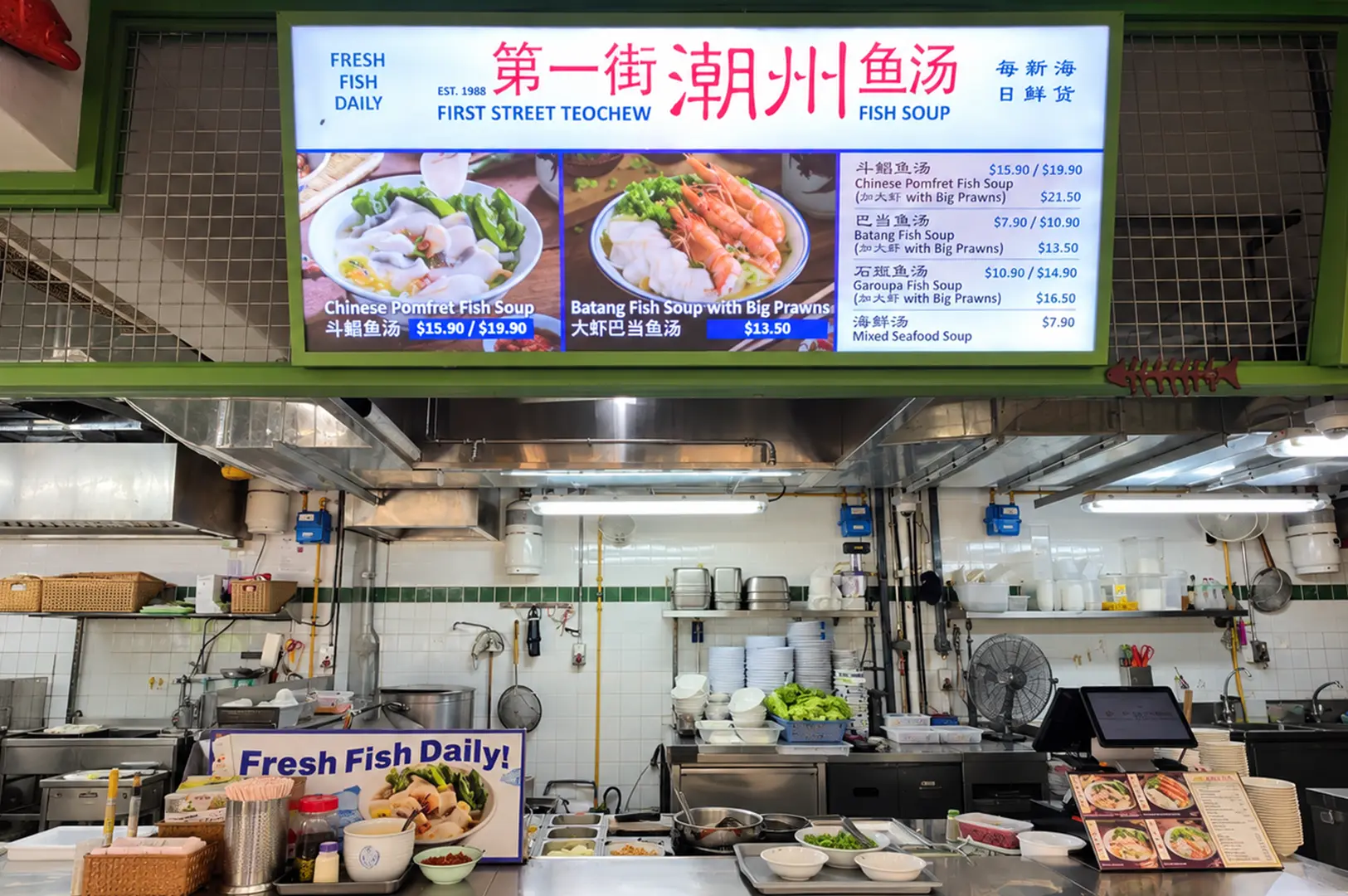 First Street Teochew Fish Soup stall with a bright menu board and open kitchen preparation area.