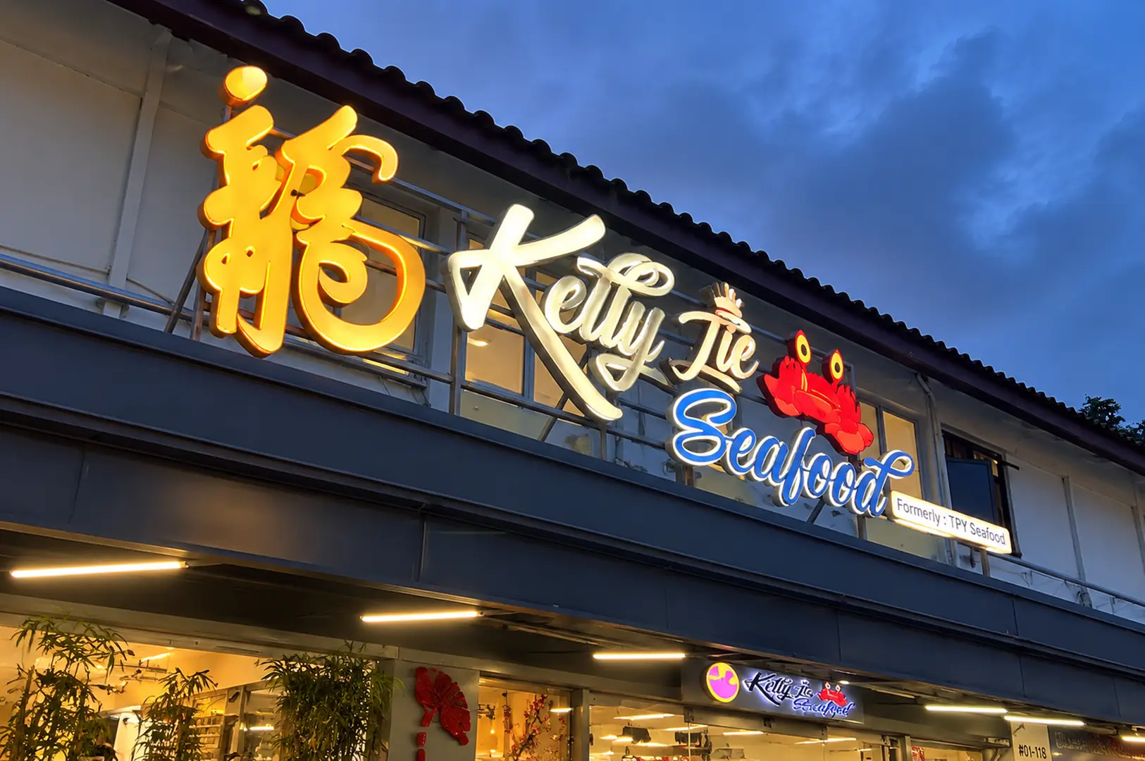Kelly Jie Seafood restaurant sign glowing against a blue evening sky above the restaurant entrance.