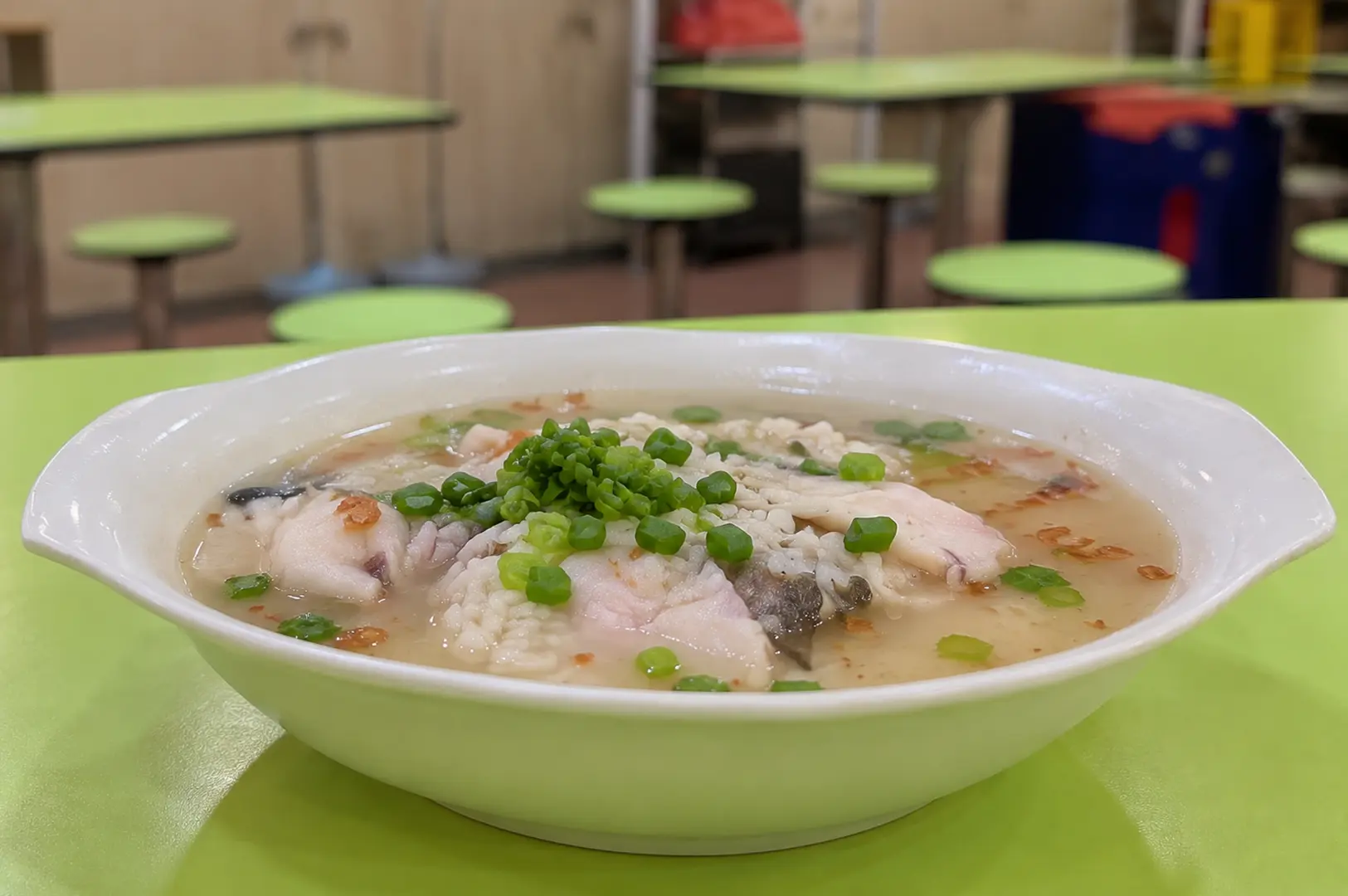 Shallow bowl of fish porridge topped with sliced fish, chopped green onions, and crispy fried shallots.