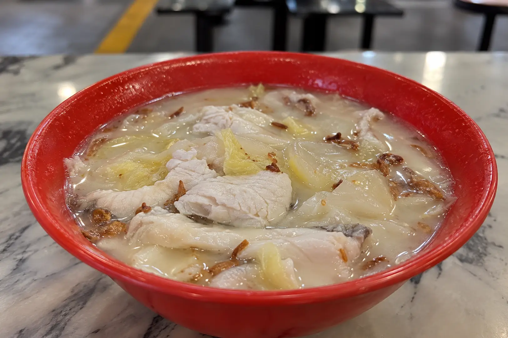 Red bowl of creamy fish soup filled with tender fish slices, cabbage, and crispy fried shallots.