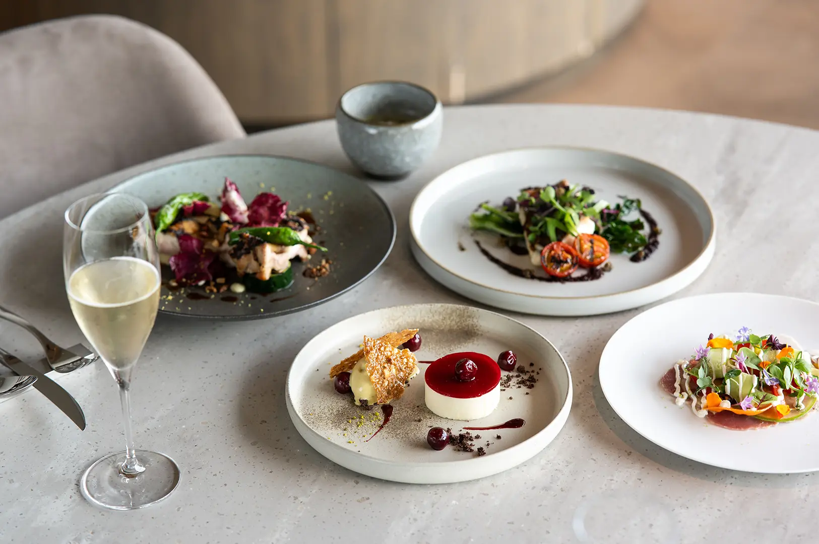 A selection of beautifully plated gourmet dishes and dessert served with wine in a refined restaurant setting.