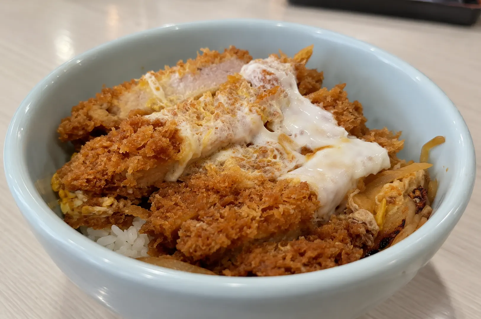 Close-up of crispy breaded katsu topped with soft egg over rice in a light blue bowl.
