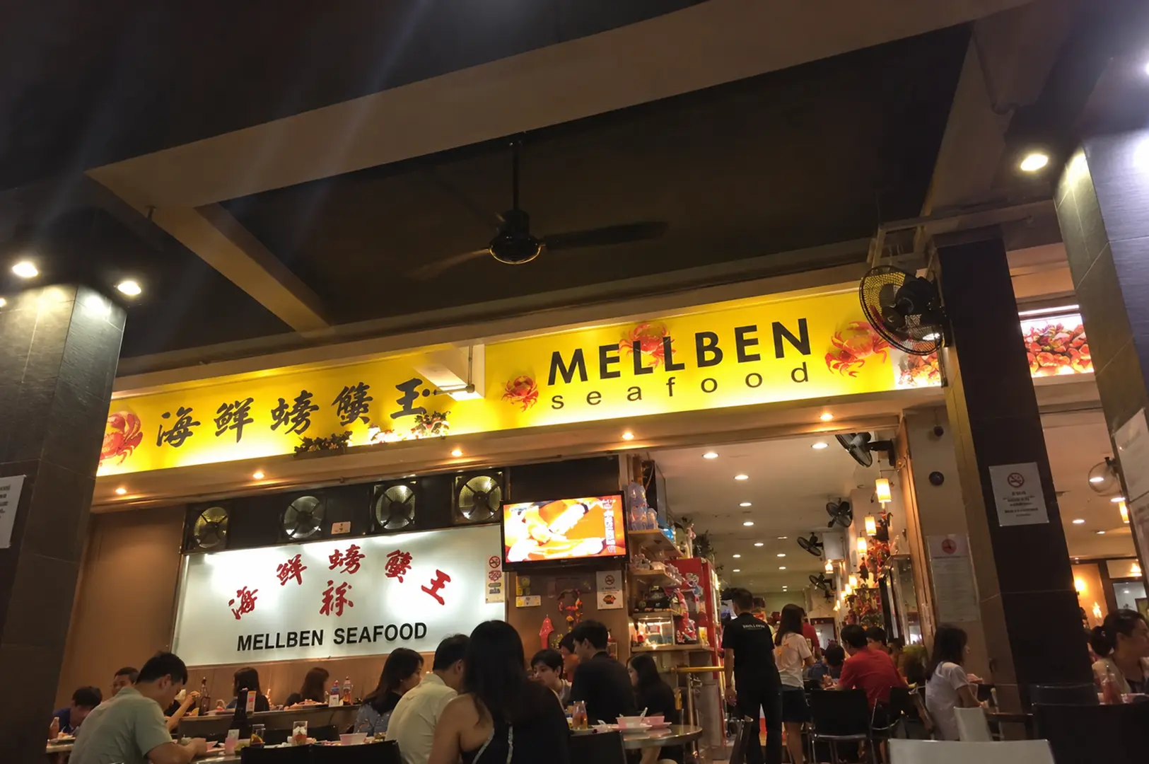Mellben Seafood restaurant entrance with a bright yellow sign, Chinese lettering, and diners seated inside.