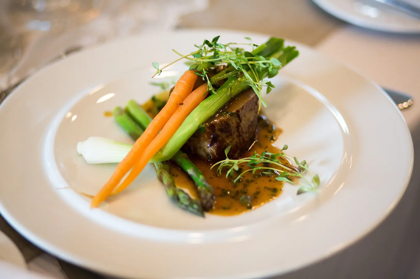 A gourmet beef main course served with fresh vegetables, herbs, and sauce on a white plate.