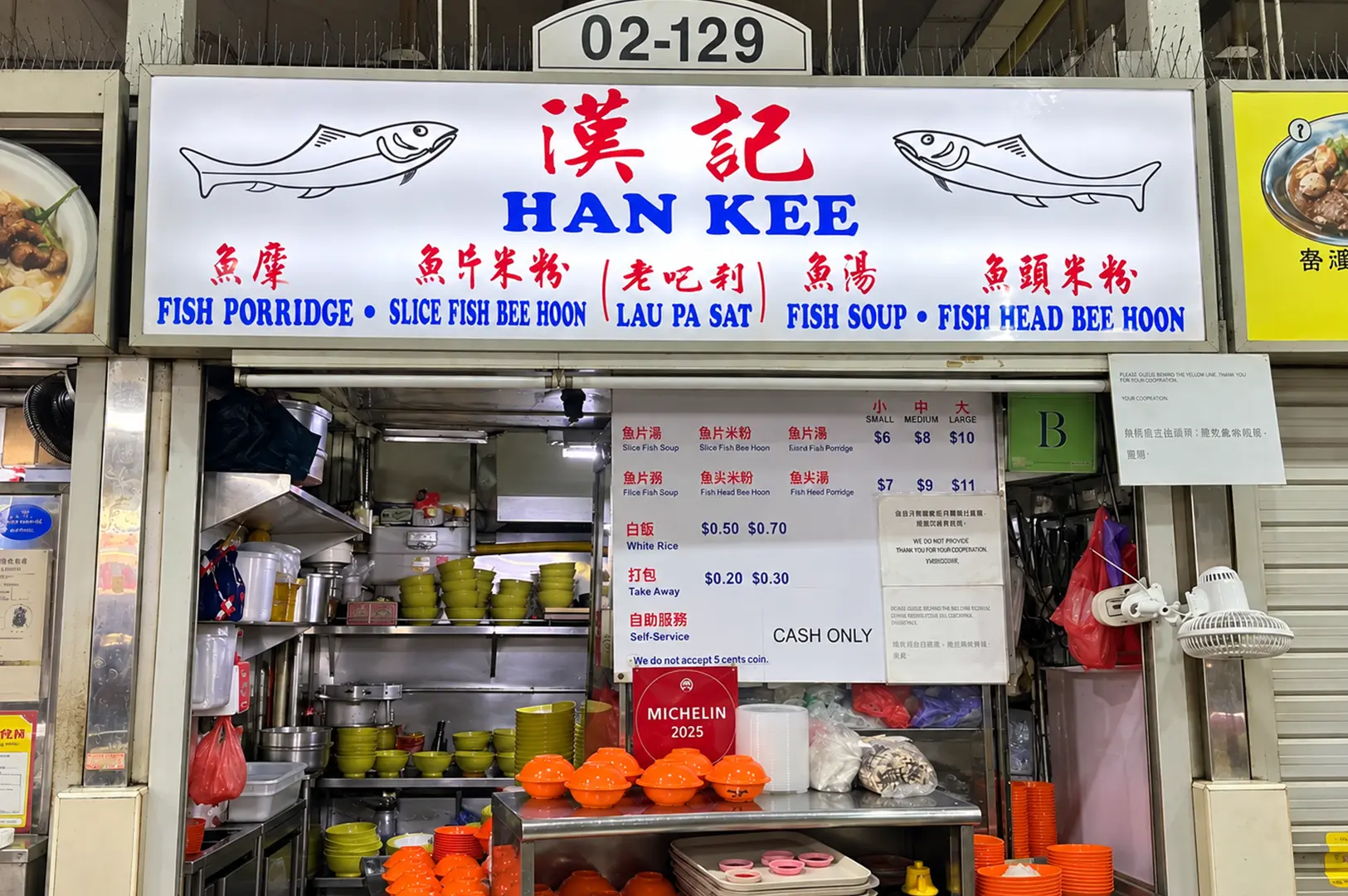 Han Kee fish soup stall displaying its menu, colorful bowls, and busy food preparation area.