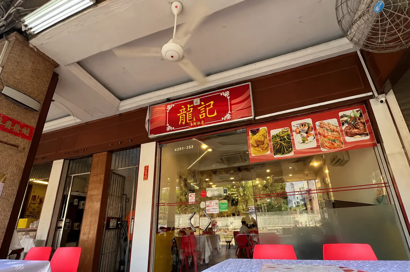 Long Kee seafood restaurant storefront with a red sign, glass entrance, and red chairs outside.