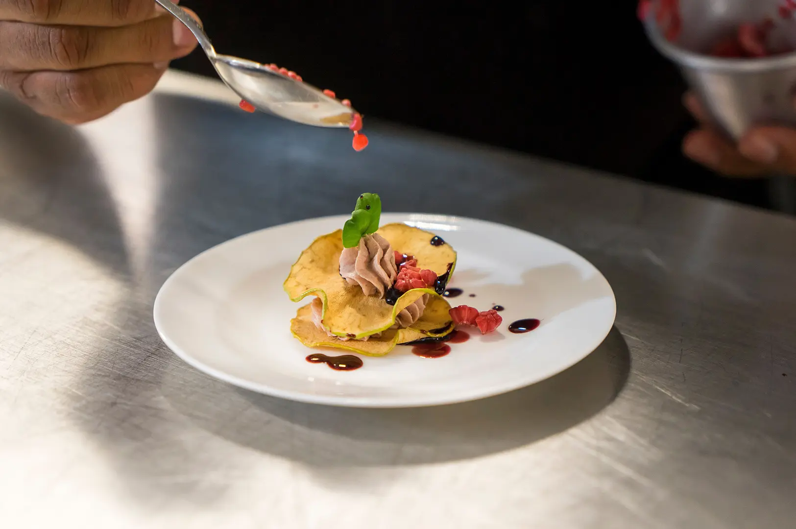 A chef carefully garnishes an artistic dessert on a white plate during fine-dining preparation.