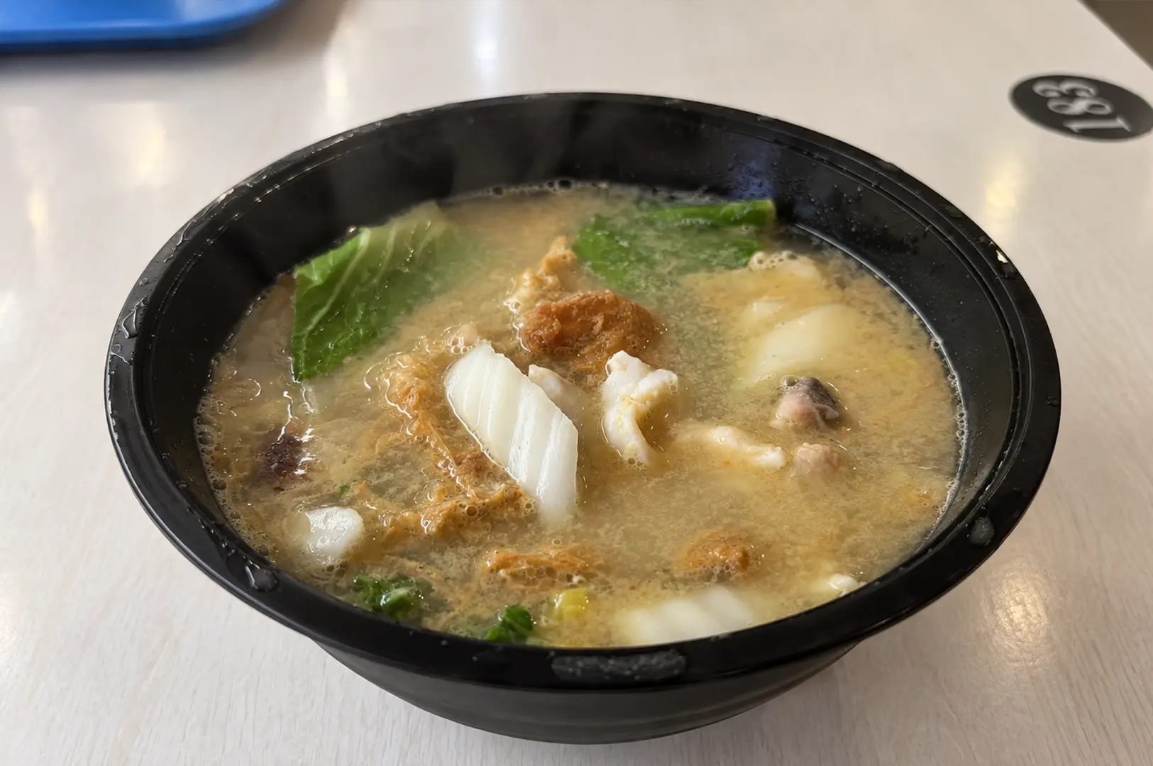 Black bowl of fish soup with white fish slices, vegetables, tofu, and a savory-looking broth.
