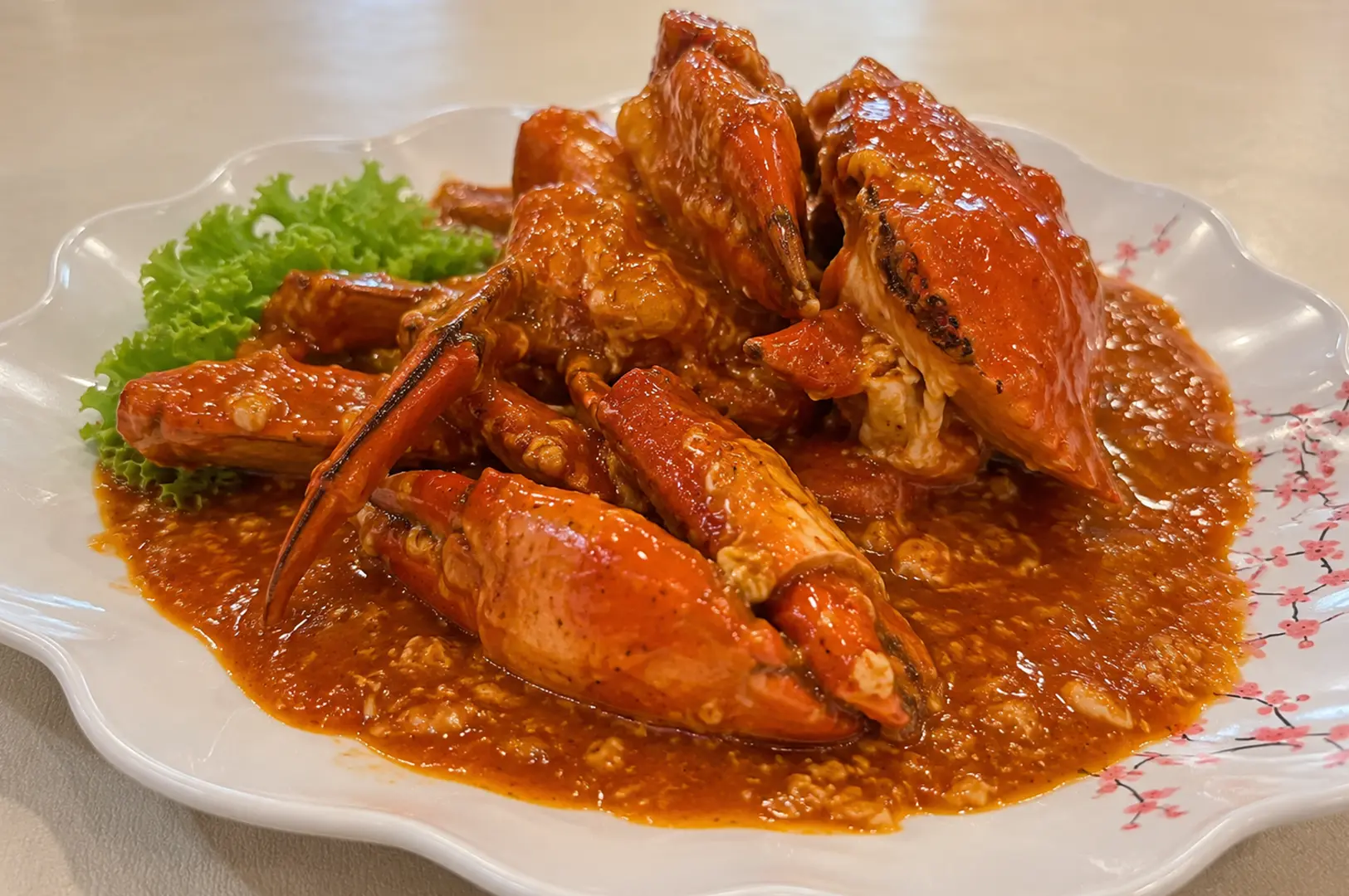 Crab pieces coated in glossy orange-red sauce, arranged on a decorative white plate with lettuce garnish.
