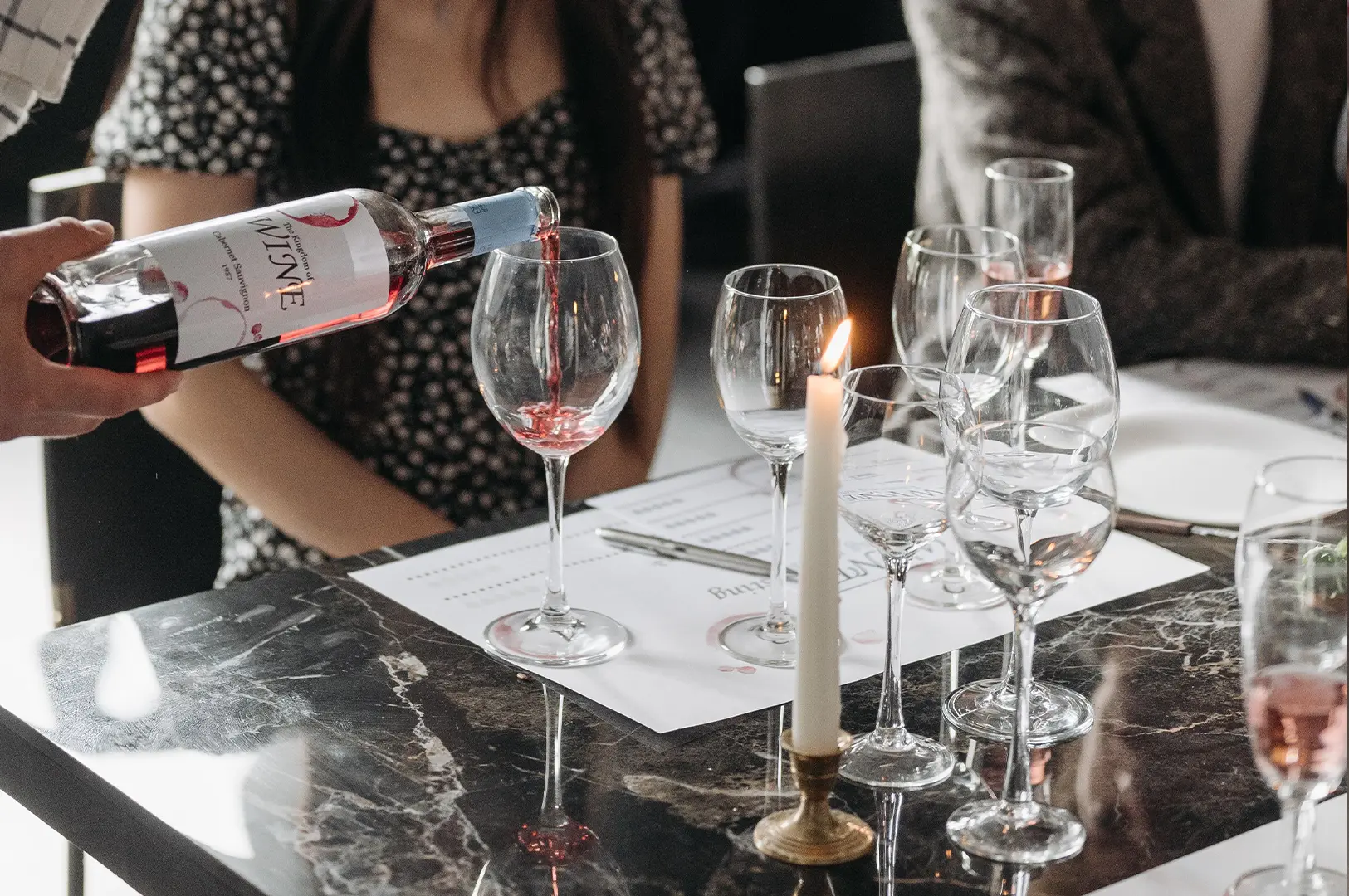 Wine being poured into elegant stemware at a formal dining table with a candlelit atmosphere.