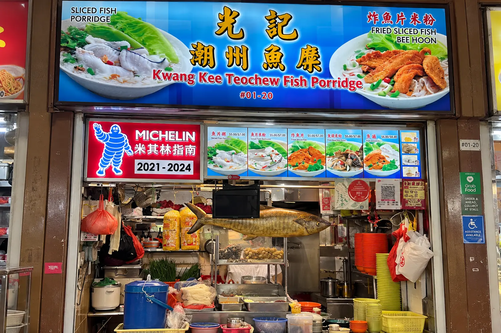 Kwang Kee Teochew Fish Porridge stall with colorful signage, menu displays, and a fish decoration above the counter.