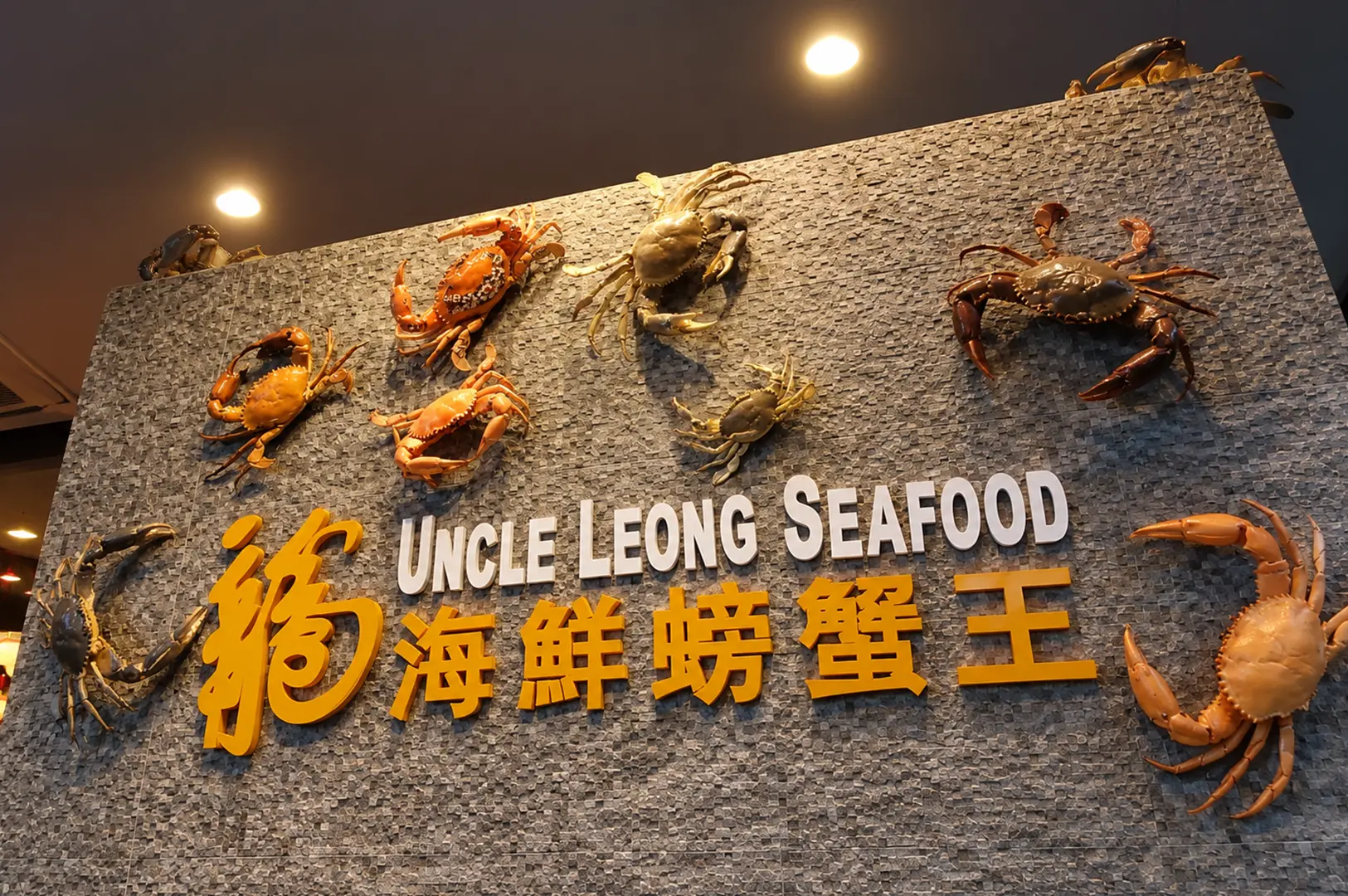 Uncle Leong Seafood sign displayed on a textured gray wall decorated with mounted crab sculptures.